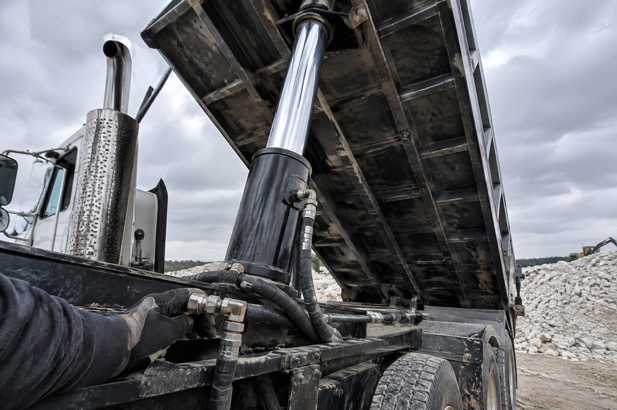 Dump truck bed raised on a telescopic hydraulic hoist cylinder, mechanic checking a fitting